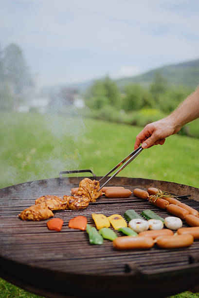 Man grilling meat and vegetables outdoors during summer party