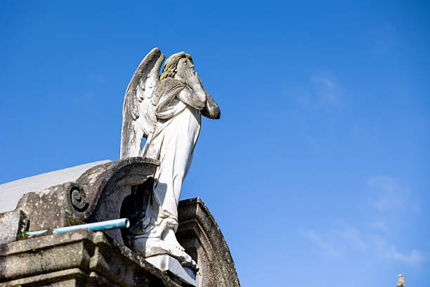 Statue of a melancholic female figure in front of a cross. Cloudy day, atmosphere of sadness.