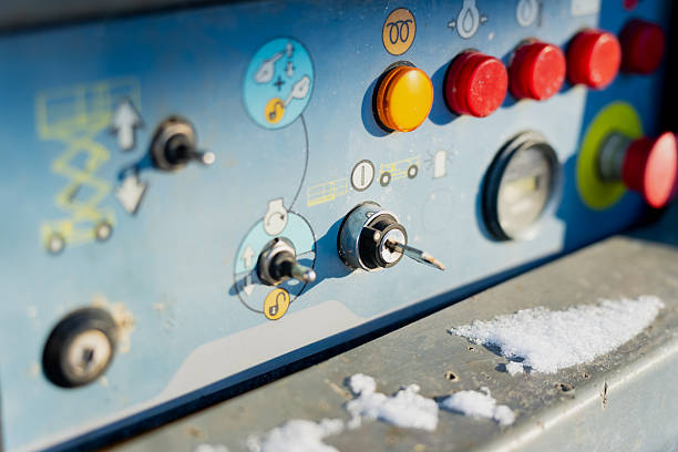 Industrial machinery control console with buttons and key switch, close up of operator panel partially covered by snow in cold outdoor conditions