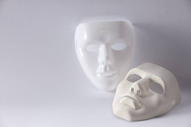 Person is hiding face behind a white mask on black background.