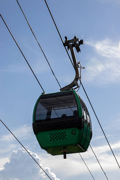 A vibrant green cable car, marked with the number 42, is seen suspended against a bright blue sky dotted with soft white clouds, symbolizing modern aerial transportation and scenic travel.