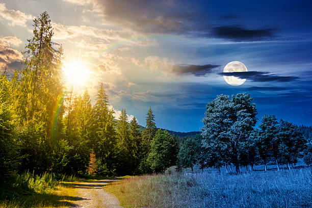 old gravel road through forest. day and night time change concept. beautiful summer landscape with sun and moon at twilight. cloud above the distant mountains. harmony and progress calendar