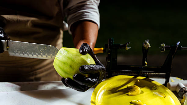Person peeling a green fruit with a knife, preparing food in a kitchen scene