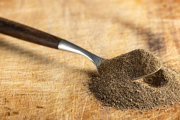 Freshly ground black pepper in a wooden spoon on rustic cutting board. Close up view.