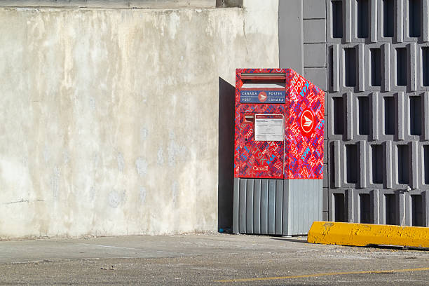 Calgary, Alberta, Canada. Jan 18, 2026. A colorful Canada Post mailbox with a vibrant red and purple graphic wrap standing against a concrete wall.