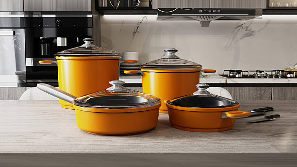 Cookware set in bright orange color is arranged on a kitchen counter. The space features modern appliances and utensils, suggesting a lively cooking atmosphere.