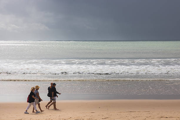 Noosa Heads, Australia - May 12, 2025: People walking along the sandy shore of Noosa Heads Beach, Sunshine Coast, Queensland, Australia against a dark, moody sky and horizon.