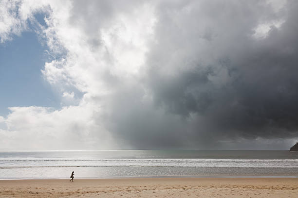 Silhouette of a lone woman walking along Noosa Heads Beach with a dark moody sky on the horizon on the Sunshine Coast, Queensland, Australia.