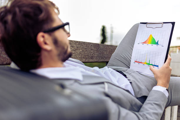 Young businessman lying on a bench outdoors, reviewing a paper report. Ideal for business, professional lifestyle, urban work, and productivity concepts.