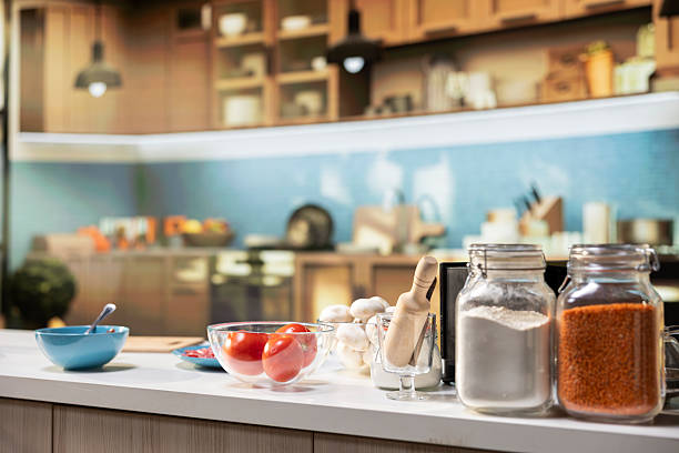 Modern kitchen interior ready for homemade pizza preparation. Counter displays fresh ingredients like red bell pepper and sauce alongside utensils and baking tools for home cooking.