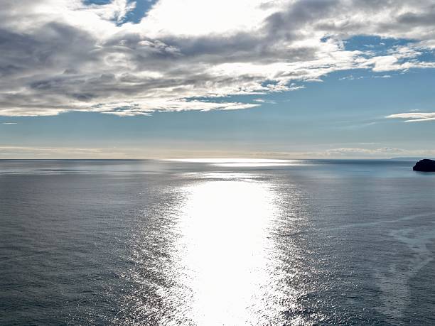 glittering sunlight path across calm sea, bright reflective ribbon stretches toward distant horizon