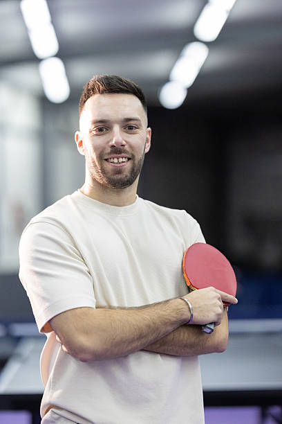 Young man holding a table tennis paddle with crossed arms, smiling confidently