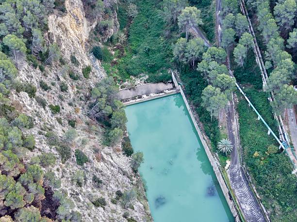 Cliffside water intake pool beside turquoise reservoir, concrete channel, service path, maintenance access,