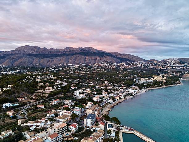 Aerial turquoise horizon with quiet pier extending into calm sea at dusk, coastal homes and lowrise resorts