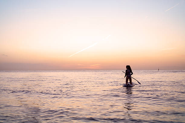 Serene young woman paddle boarding at sunset on ocean during summer vacation
