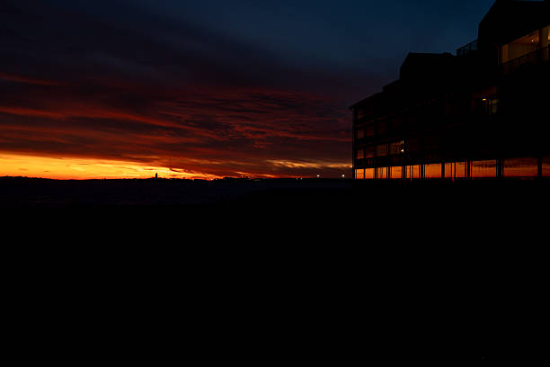 The vibrant hues of a sunset paint the sky with fiery oranges and reds, casting a dramatic silhouette of a building against the twilight