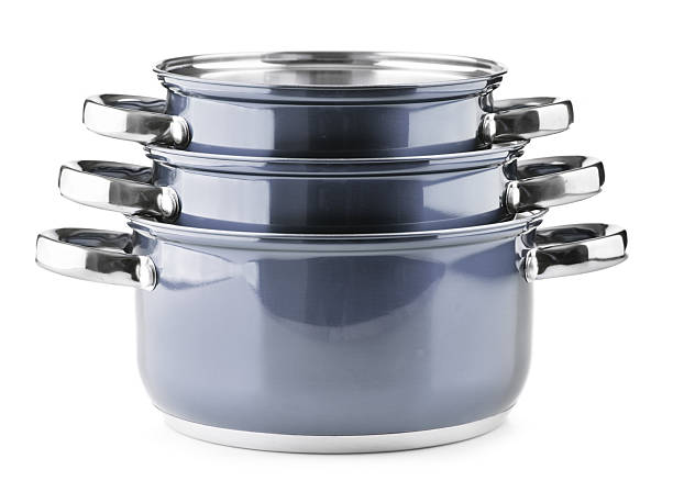 Two metal pots with shiny lids stand on the kitchen stove, the front one of which is in focus and reflects the kitchen interior. The blurred background emphasizes the homely atmosphere of cooking and the luster of the utensils.