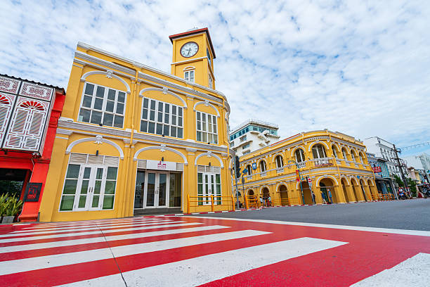 Phuket,Thailand-1 Dec 2024:Vibrant yellow Sino-Portuguese buildings and a clock tower at a street intersection in the historic Phuket Old Town, a popular Thai tourist spot.