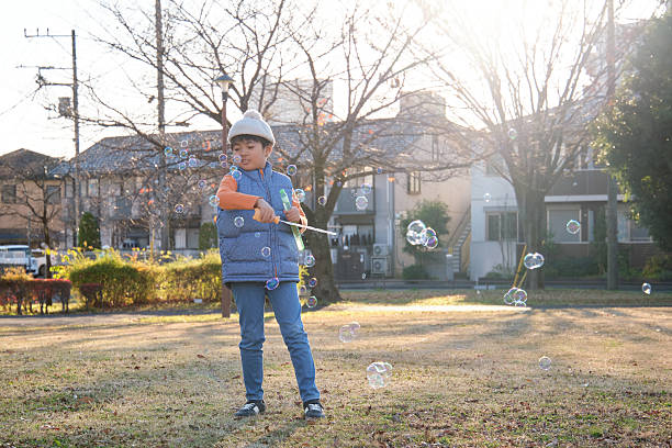 Young Asian boy blowing soap bubbles in an outdoor park during autumn