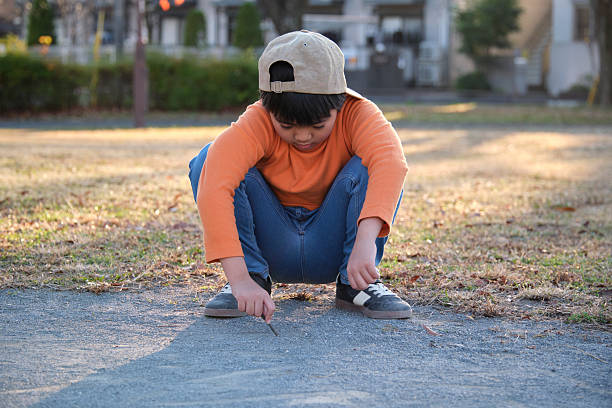 Boy concentrating while creating designs on the ground with a stick in a park
