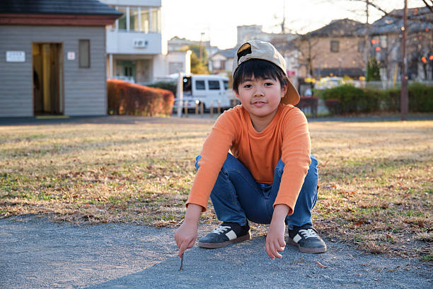 Japanese boy drawing on a dusty patch of ground with a stick in a local park