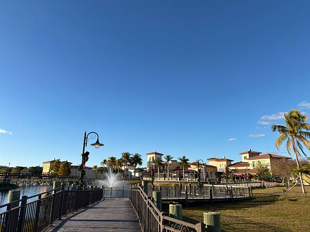 Estero - Fort Myers Beach, Florida, United States of America - January 1, 2026: Lakeside boardwalk to shops and a fountain at Gulf Coast Town Center, festive Christmas decorations and palm trees under warm, sunny Florida skies — tranquil waterfront plaza