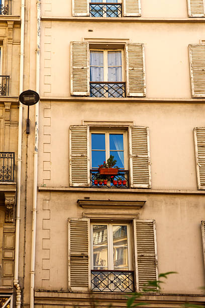 Haussmannian building facade with traditional windows, open shutters, and flower boxes in Paris, France