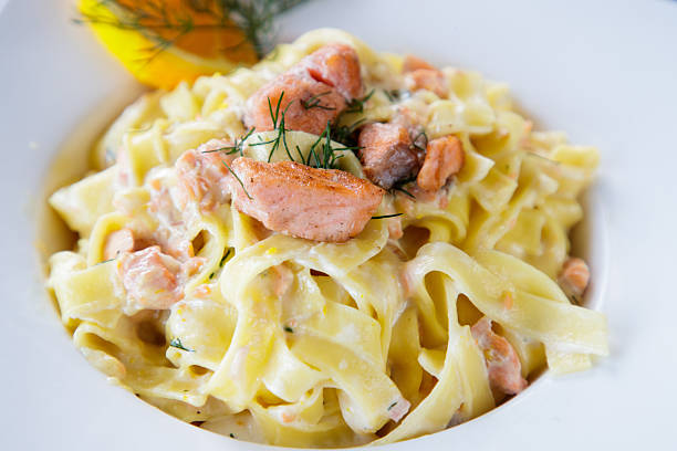 Pasta tagliatelle with salmon in white sauce served with lemon slice in deep plate, close-up, full frame