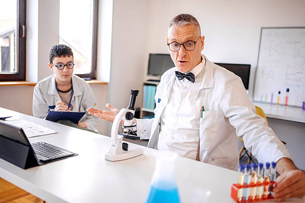 Teacher and student working on project together in school laboratory using microscope and laptop for research