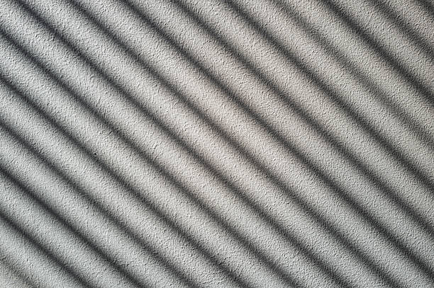 Rough cement wall in grey color covered by shadow in diagonal stripped lines from the sunlight through the window.