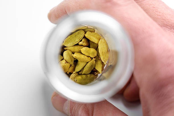 Cardamom pods in glass jar on rustic wooden background. Spices from directly above, selective focus.