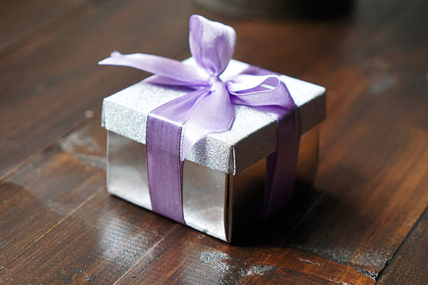 Sparkling silver gift box with lavender ribbon bow placed on rustic wooden tabletop