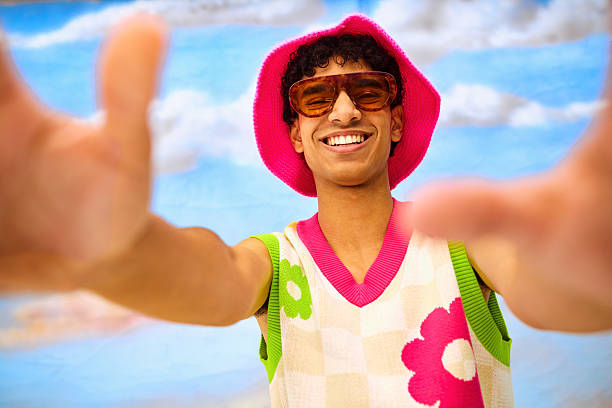 Young man smiling while reaching hand out to camera in casual retro outfit