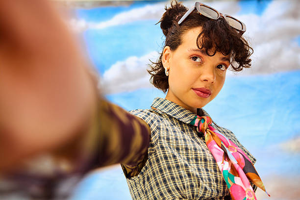 Young woman posing for a selfie in a studio against a blue sky background