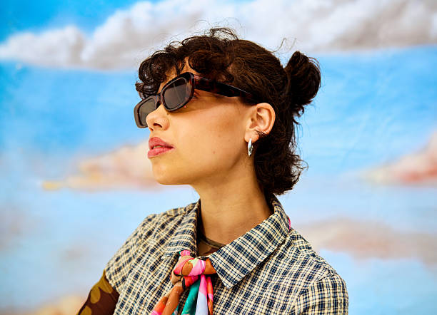Young adult woman wearing sunglasses and a patterned shirt in a studio setting