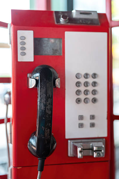 Classic style telephone booth or payphone in red color, the iconic of telecommunication system. Close-up and selective focus at the phone part.