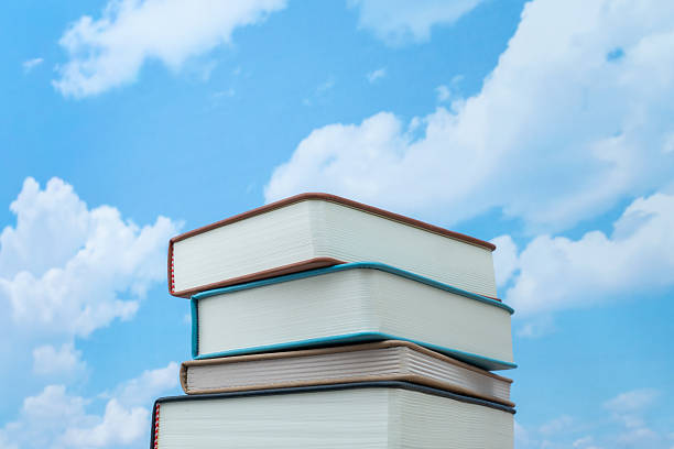 A low-angle shot of a stack of books reaching toward a bright blue sky. Higher education, limitless knowledge, and intellectual growth concept.