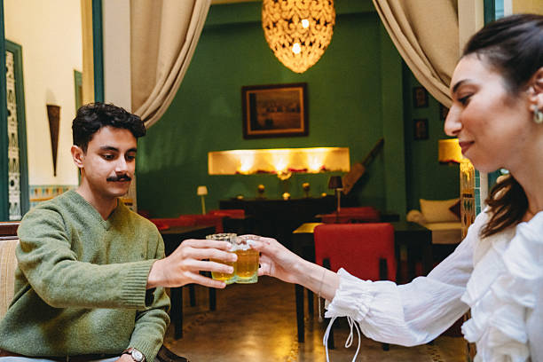 Happy young couple clinking tea glasses, enjoying traditional Moroccan hospitality and culture in a vibrant Marrakech restaurant