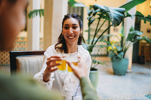 Two women sharing a moment, smiling and toasting with glasses of mint tea inside a beautiful Moroccan riad