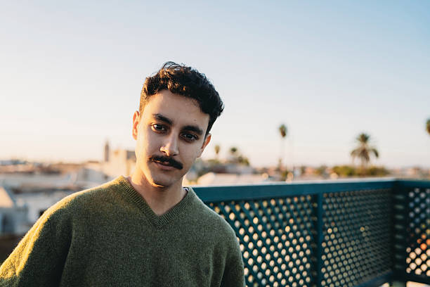 Young adult man with mustache smiling on a rooftop in Marrakech during golden hour, city view in background