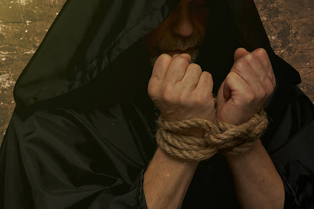 Bound monk hands holding rosary on dark background.