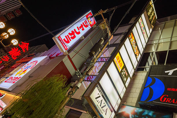 Osaka, Japan - November 5, 2023: View of brightly lit storefronts and illuminated signs in the Dotonbori district at night, with visible Japanese writing, commercial logos, and building facades.