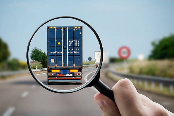 A magnifying glass focusing on a shipping container transported by truck, representing freight distribution.
