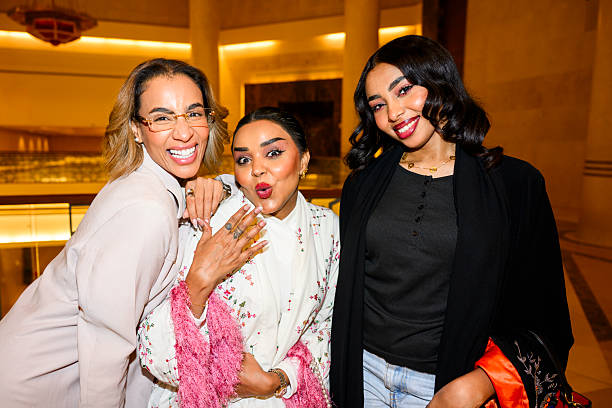 Three smiling adult women friends standing close together, laughing and making playful faces while posing for a casual group moment indoors, highlighting their strong bond