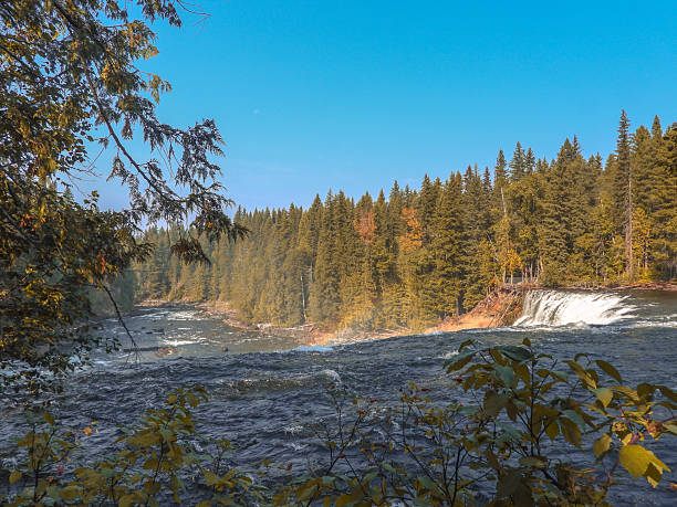 River waterfall surrounded by evergreen forest in British Columbia, Canada. Mist rises above the flowing water in early autumn.