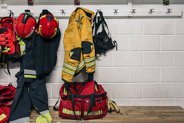 Protective clothing and gear hanging on hooks and placed on bench in fire station locker room, ready for emergency response