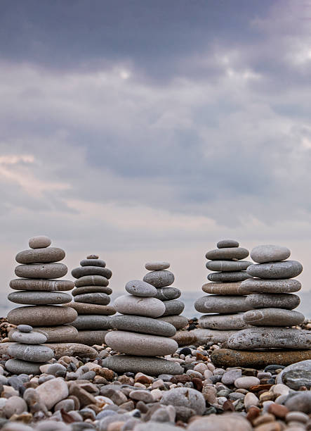 Multiple towers of smooth, balanced sea stones (cairns) on a grey pebble beach