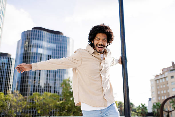 Smiling young man with afro enjoying carefree joy and confidence outdoors against a modern city skyline on a sunny day