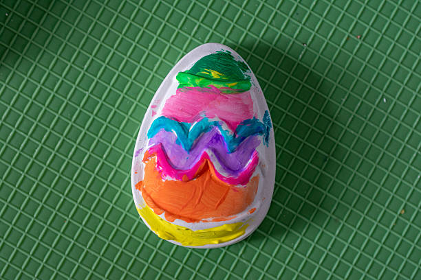 Painted egg with a rainbow stripe on it. The egg is sitting on a green surface.