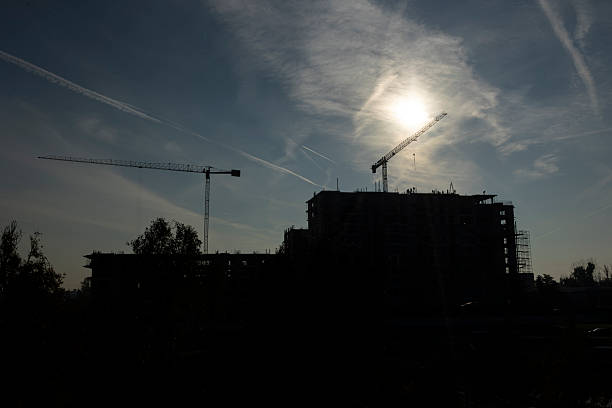 Large tower cranes used for installing roof over unfinished concrete building. Heavy construction machinery arms extended over high rise building against bright sky, concept of urban growth